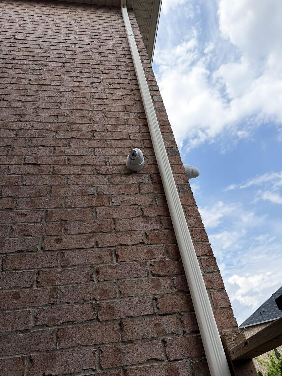 Dome camera fitted neatly under the roofline of a brick home