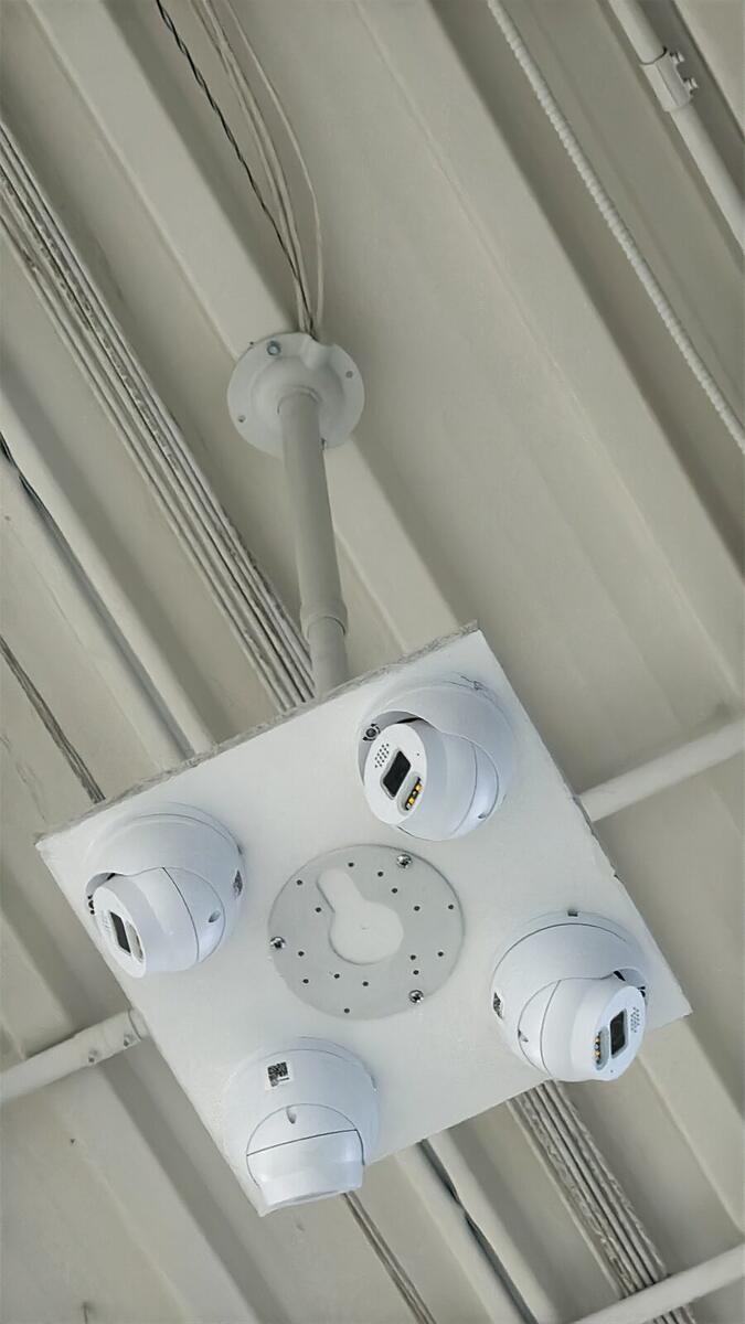 Four security cameras mounted on a ceiling plate in a warehouse