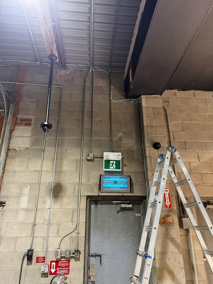 Camera and conduit run installed along a warehouse wall beside an exit door