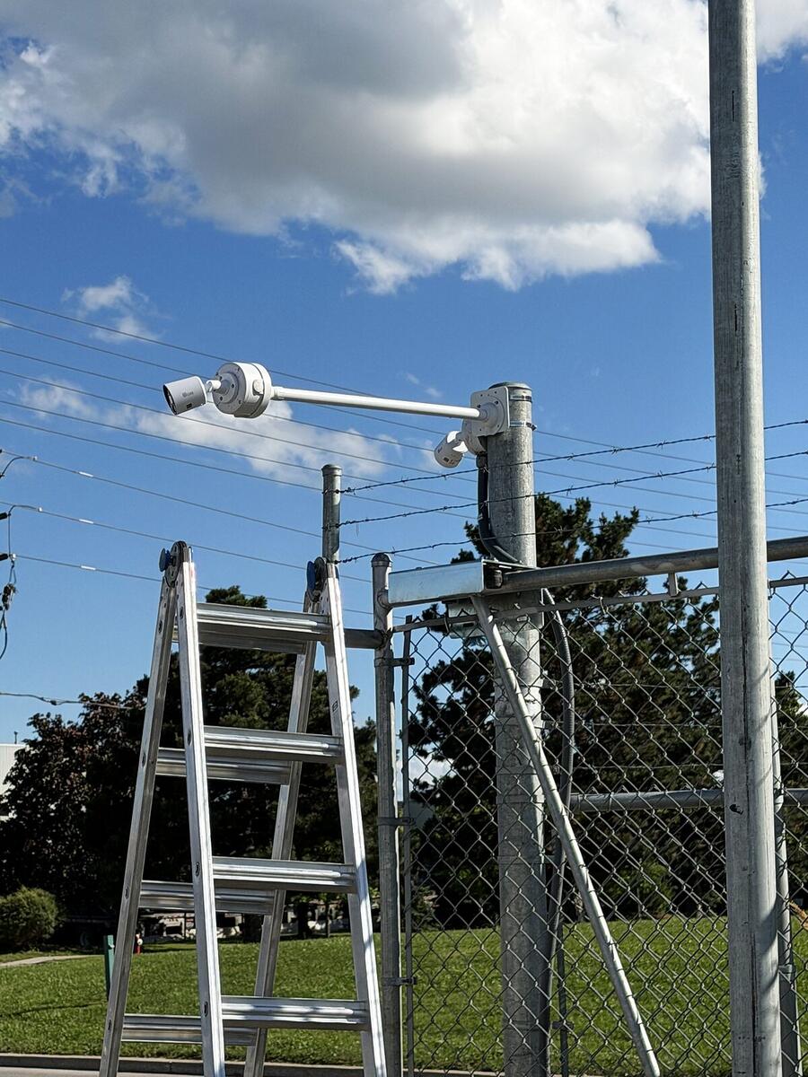 Security cameras mounted on a pole above a fenced commercial yard